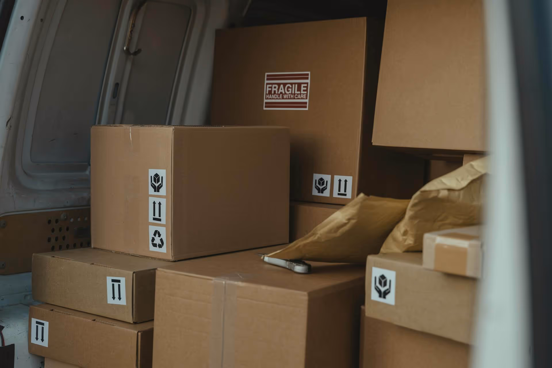 Stacked cardboard boxes inside a delivery van, one marked 'Fragile Handle With Care.'