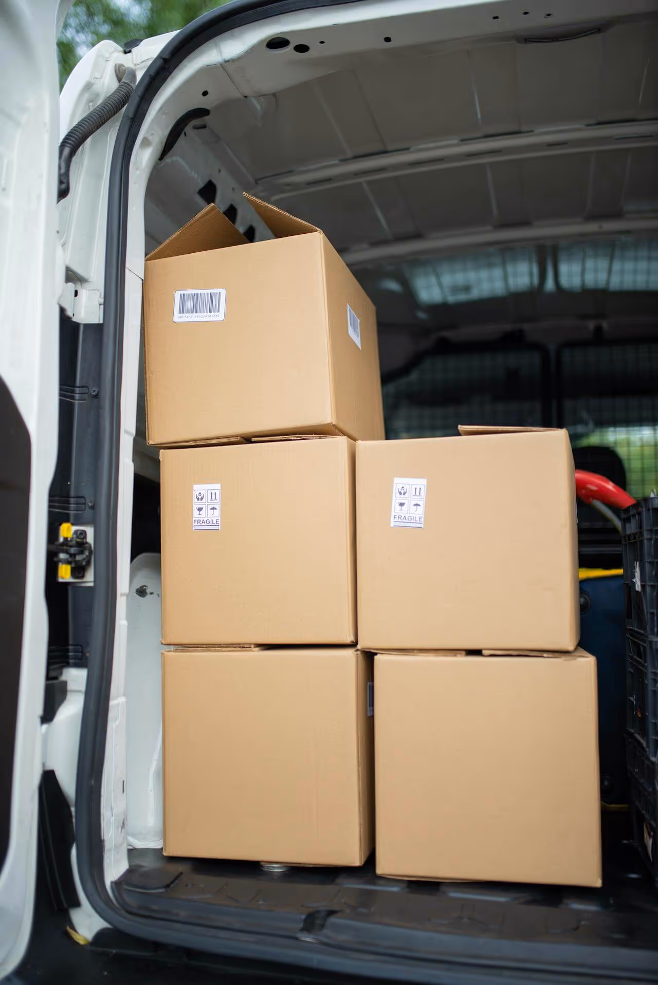 Five cardboard boxes stacked inside the back of a white delivery van, some labeled fragile.