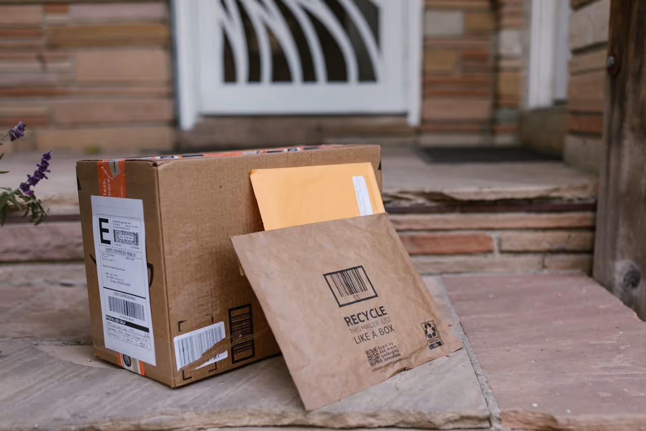 Cardboard box and padded mailer with envelope placed on a stone doorstep in front of a house door.