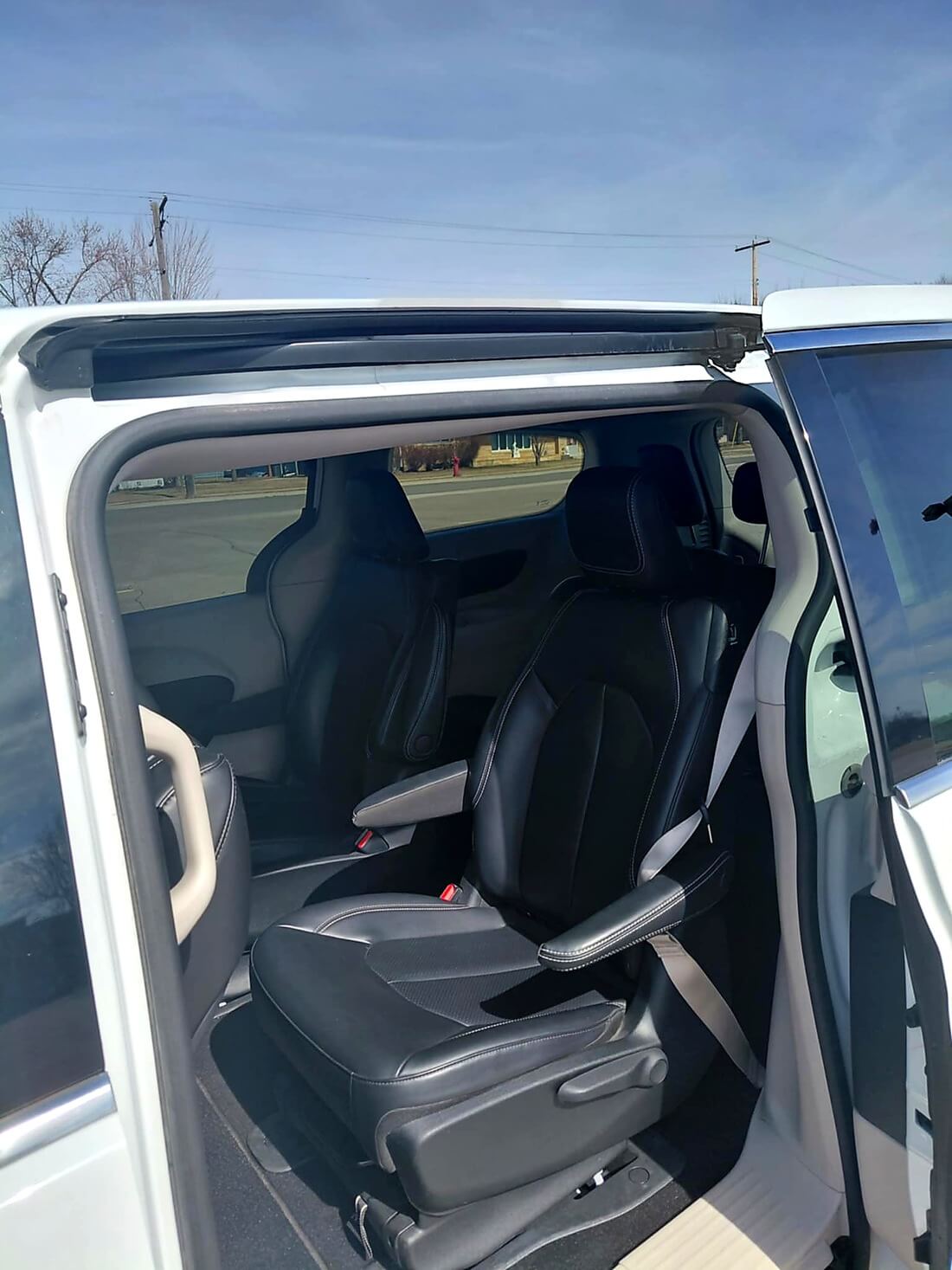 Open side door view showing black leather captain seats inside a white minivan under a clear sky.