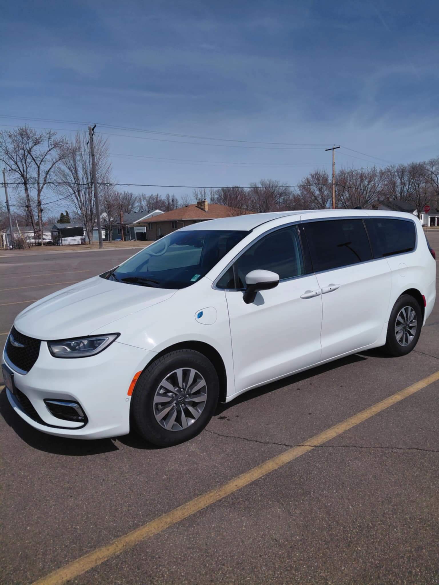 White Chrysler minivan parked in an empty lot under a clear blue sky.